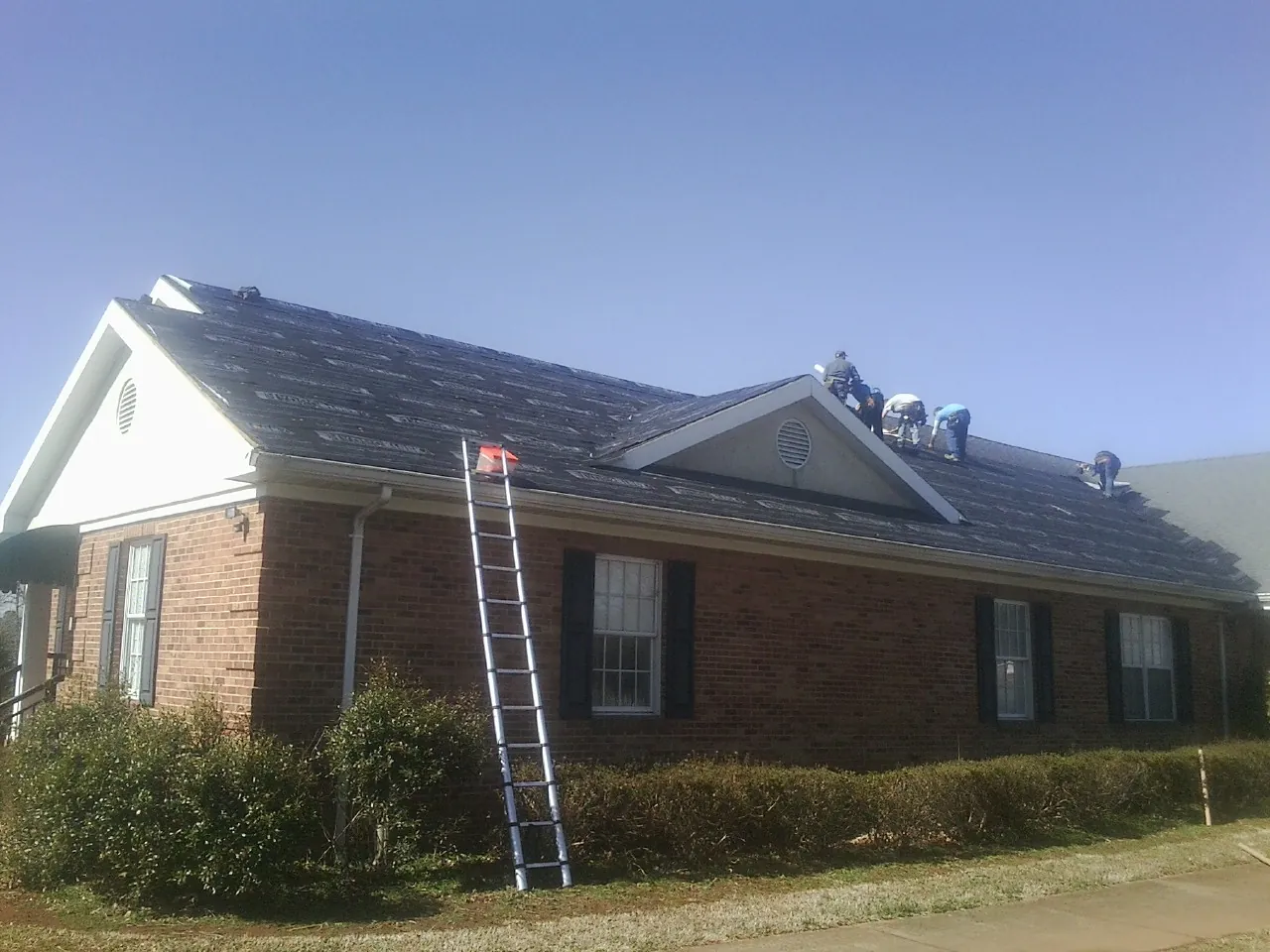 Crew tearing shingles off a brick ranch roof with a ladder set — Metal Roof Repair work by our crew in Soledad