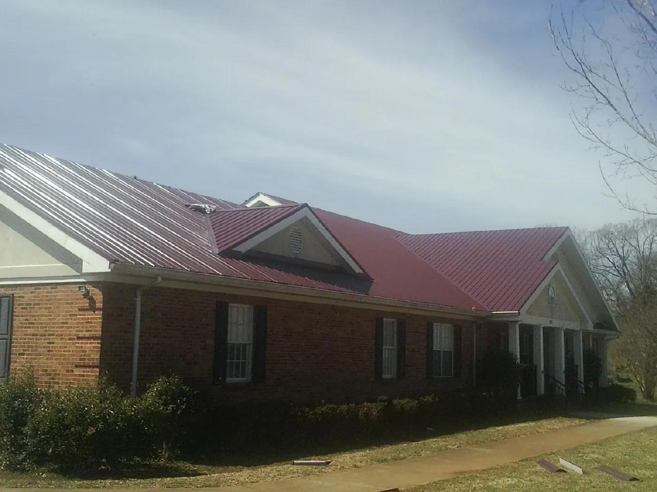 Red metal roof with gabled entries on a long brick building, from a Hail Damage Roof Repair job in Soledad