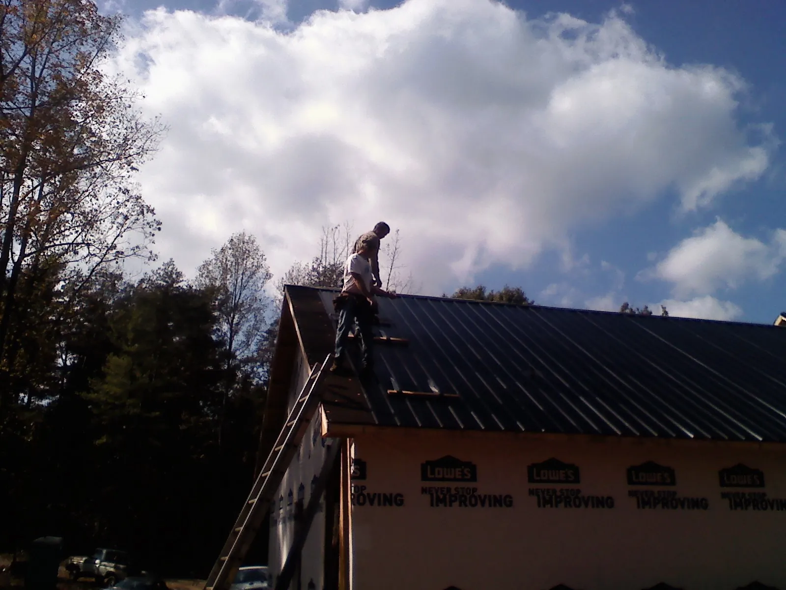 Roofer fastening dark metal panels high against a cloudy sky, from a Roof Inspection job in Soledad