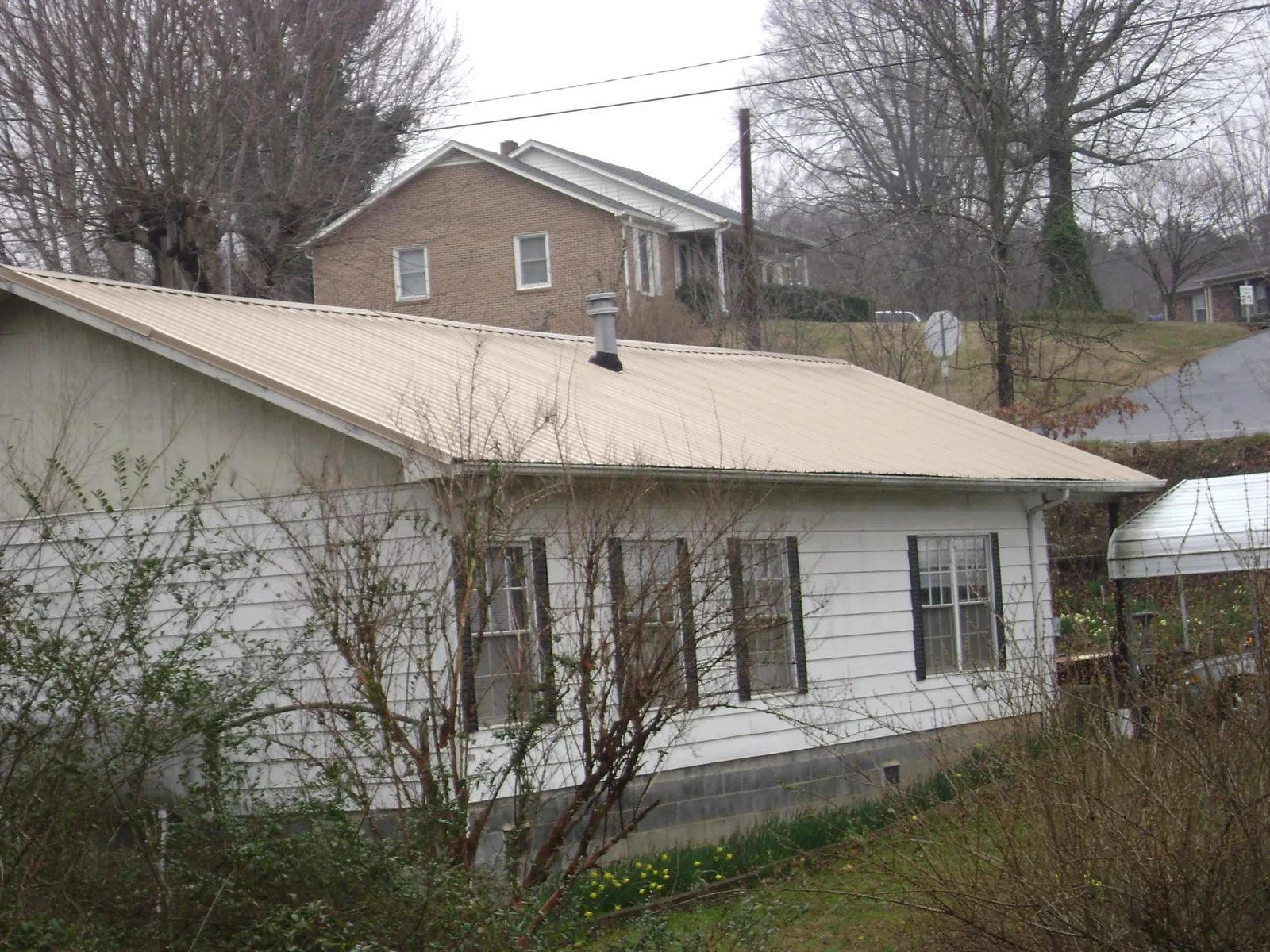 Tan metal roof on a white sided house set into a hillside — Commercial Roofing by Roofing Brothers in Soledad
