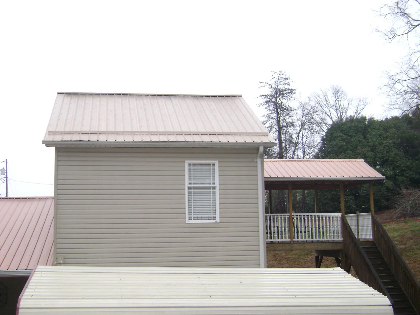Tan metal roofs on a two story addition and attached porch, from a Roof Replacement job in Soledad